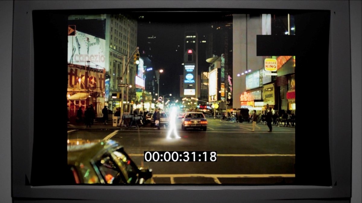 Still from Voice to Skull: a glowing figure crossing a 1980s Times Square, shown on a CRT with timecode